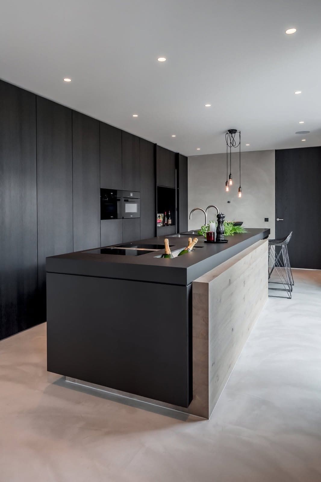 Cucina scura con isola e pavimento continuo dalle sfumature morbide