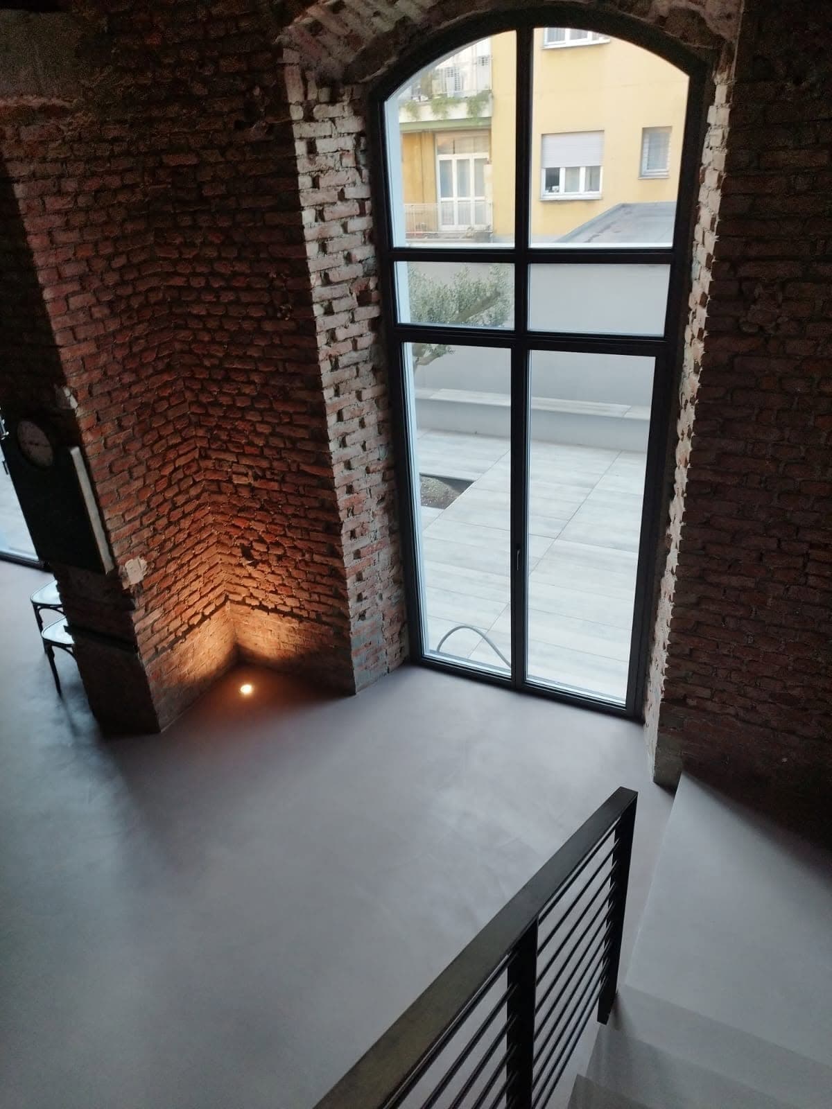 Pavimento continuo e scala in un interno con pareti in mattoni e grande vetrata