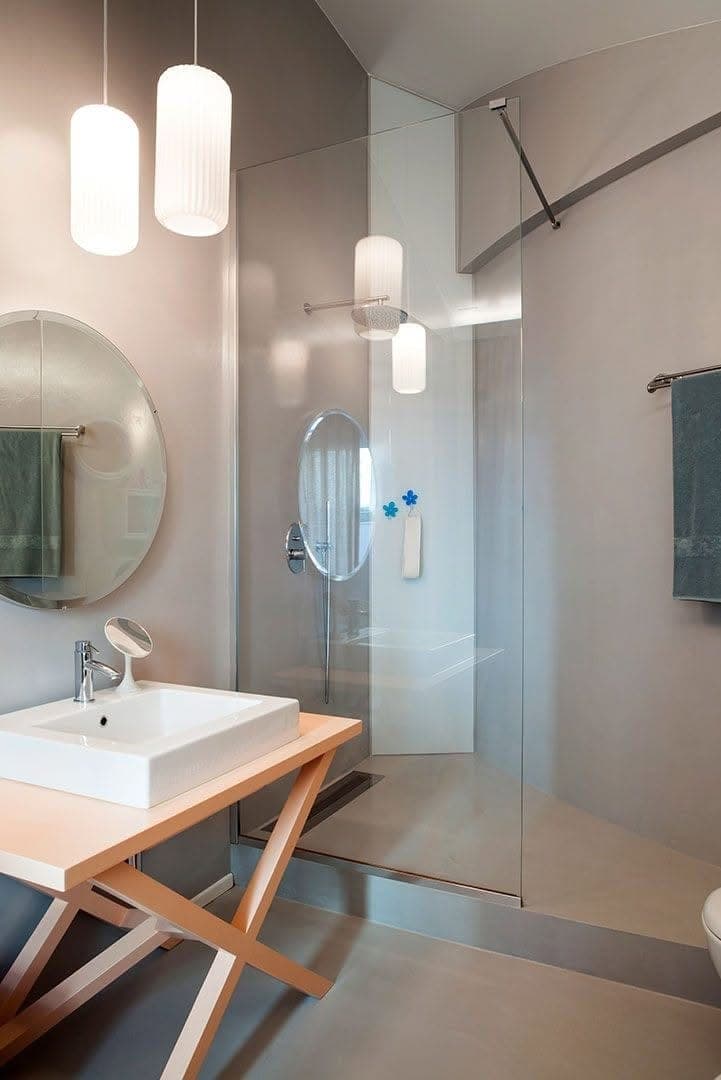 Bagno con pareti continue grigie, lavabo e doccia vetrata